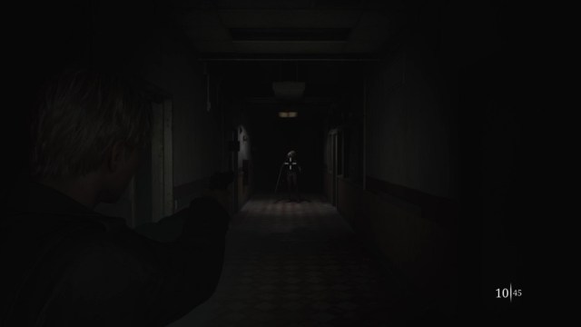 Silent Hill 2 Remake distant bubble-head nurse stands beneath a light while James aims his pistol.