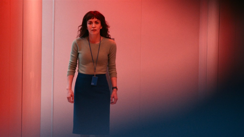 Severance - Helly stands in a hallway on the Lumon severed floor with alarms and red lights flashing, staring at Mark