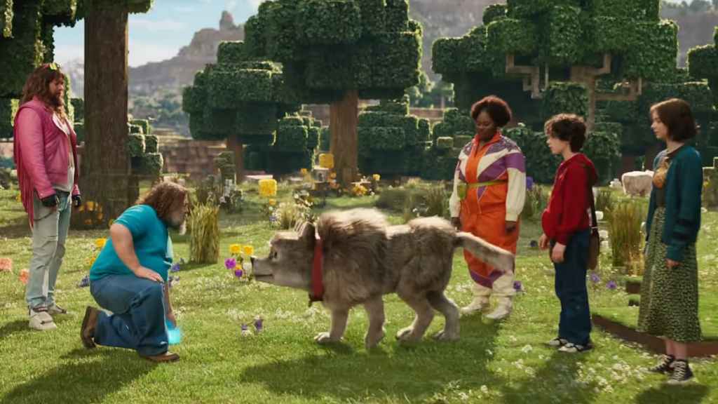 Five A Minecraft Movie characters standing in a blocky Minecraft forest with a dog. 
