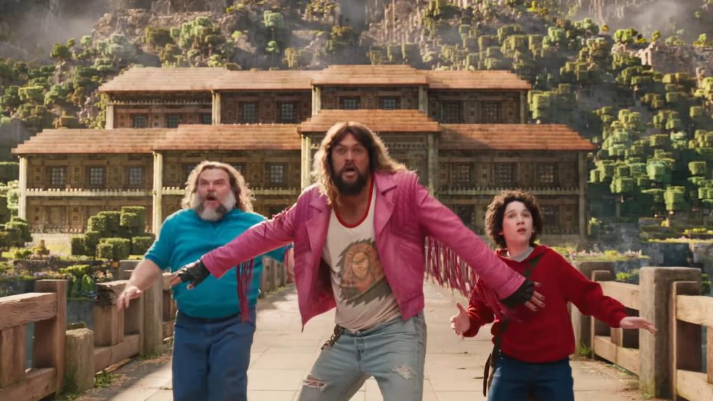 Steve, Garrett, and Henry standing on a bridge in front of a Woodland Mansion in A Minecraft Movie.