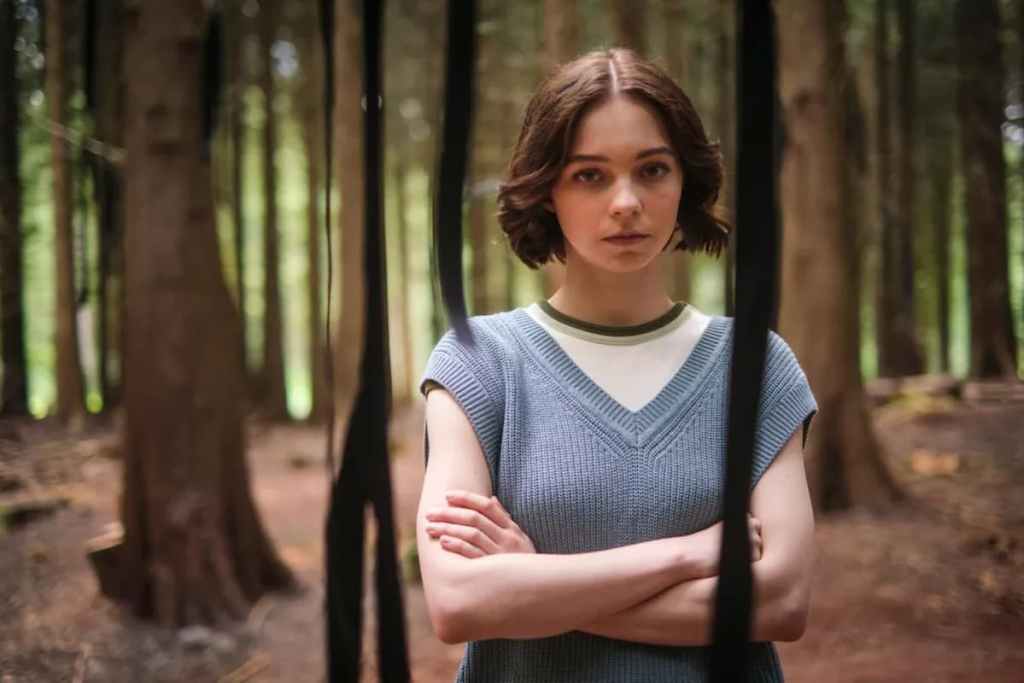 Emma Myers standing in the forest while acting in "A good girl's guide to murder."