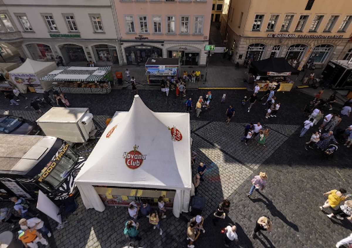 A screenshot of an event with a bunch of people in it and a white tent.