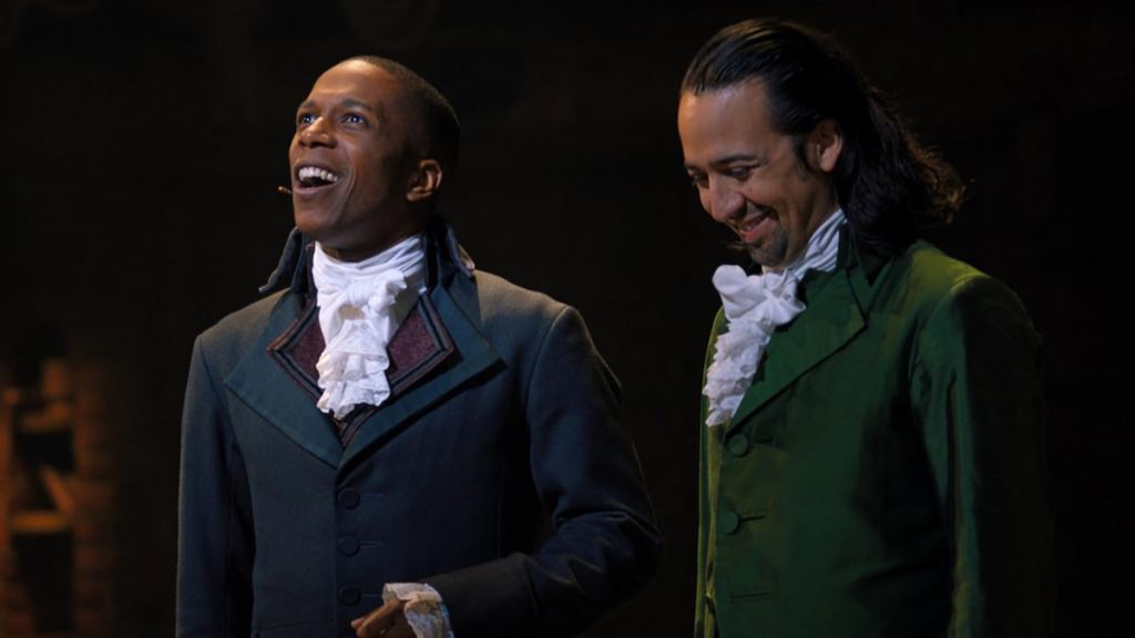 Burr smiling and looking up next to Hamilton looking down laughing in hamilton