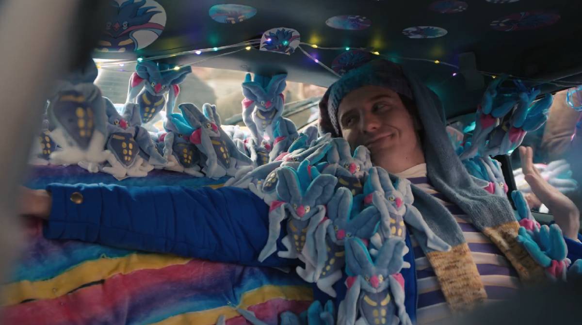 A man sits in a car surrounded by merchandise for the Pokémon Malamar